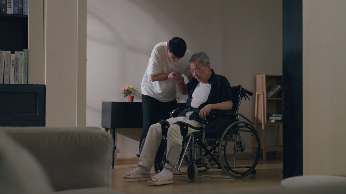 Ant-H1 Pro takılı yaşlı bir adam, tekerlekli sandalyeden kalkarken yakını tarafından destekleniyor
