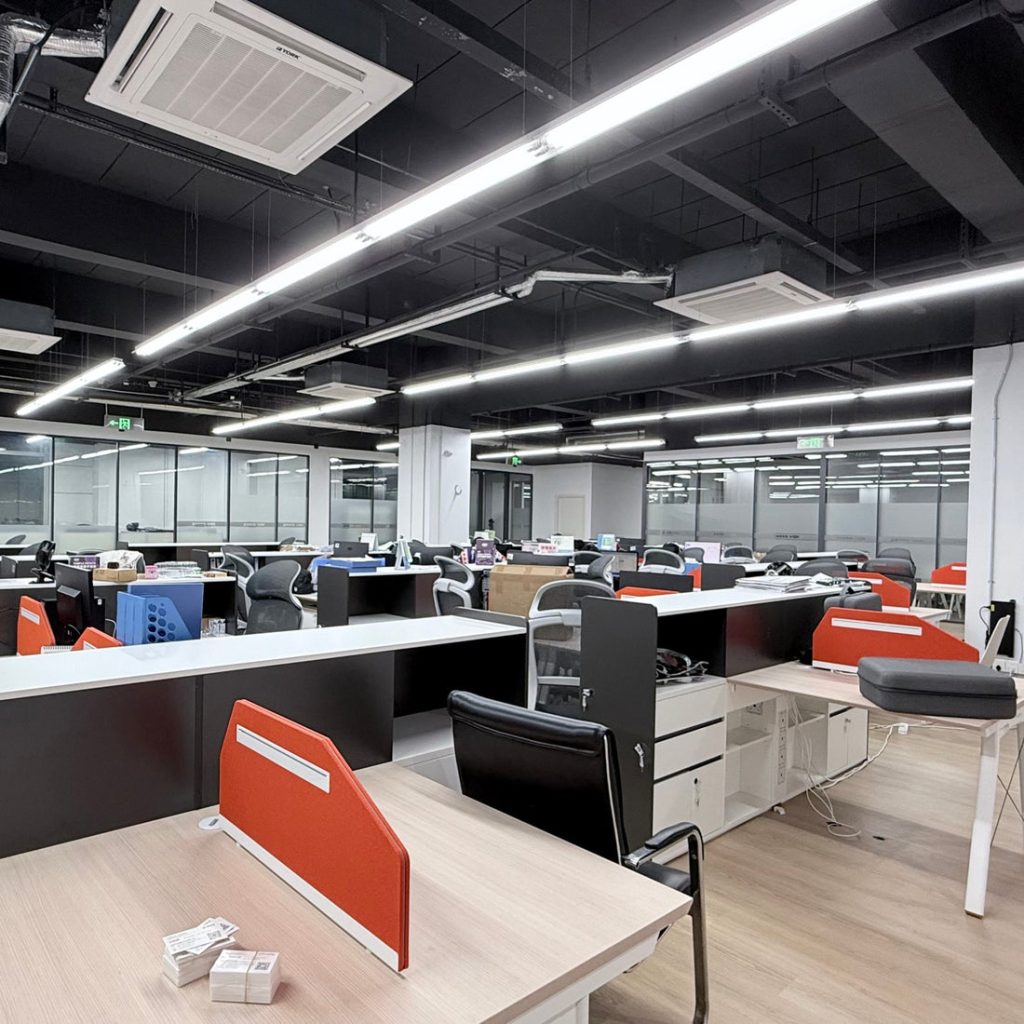 Açık ofis alanında sıralanmış çalışma masaları ve turuncu bölmeler