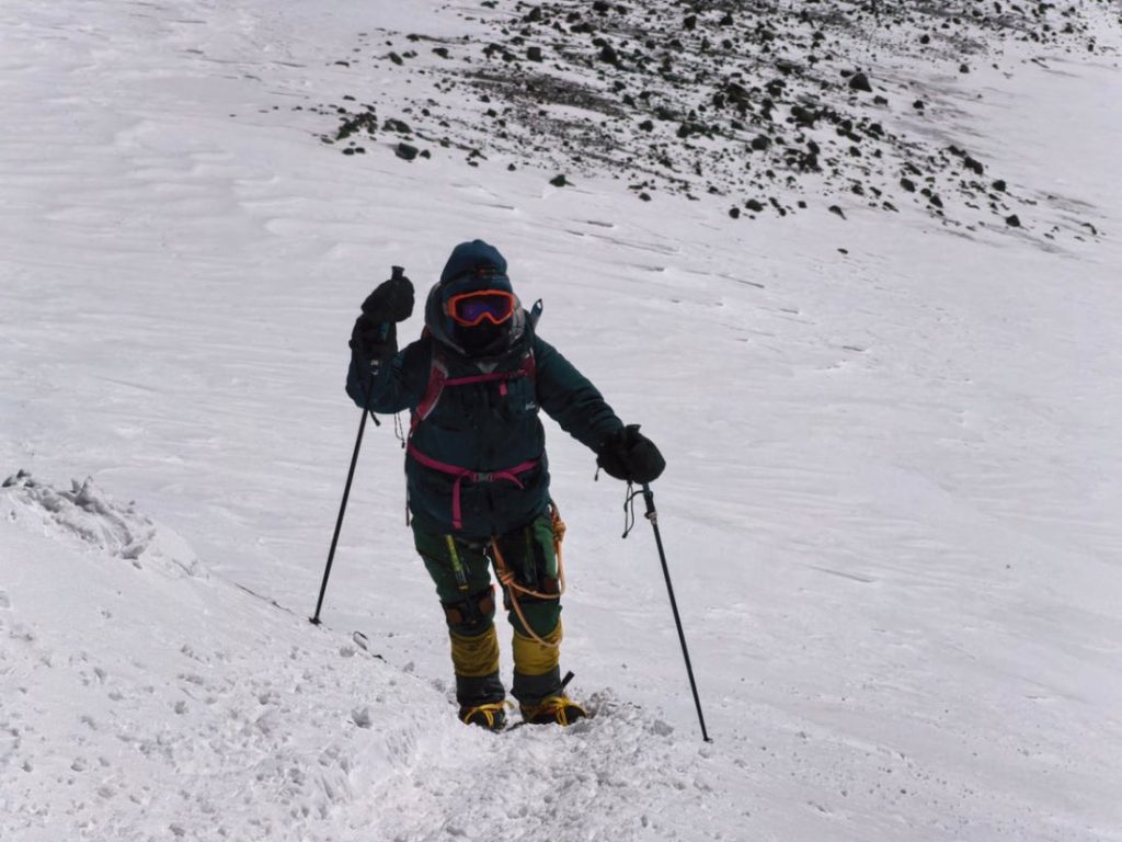 Karlı yamaçta batonlarla tırmanan, dış iskelet kullanan dağcı